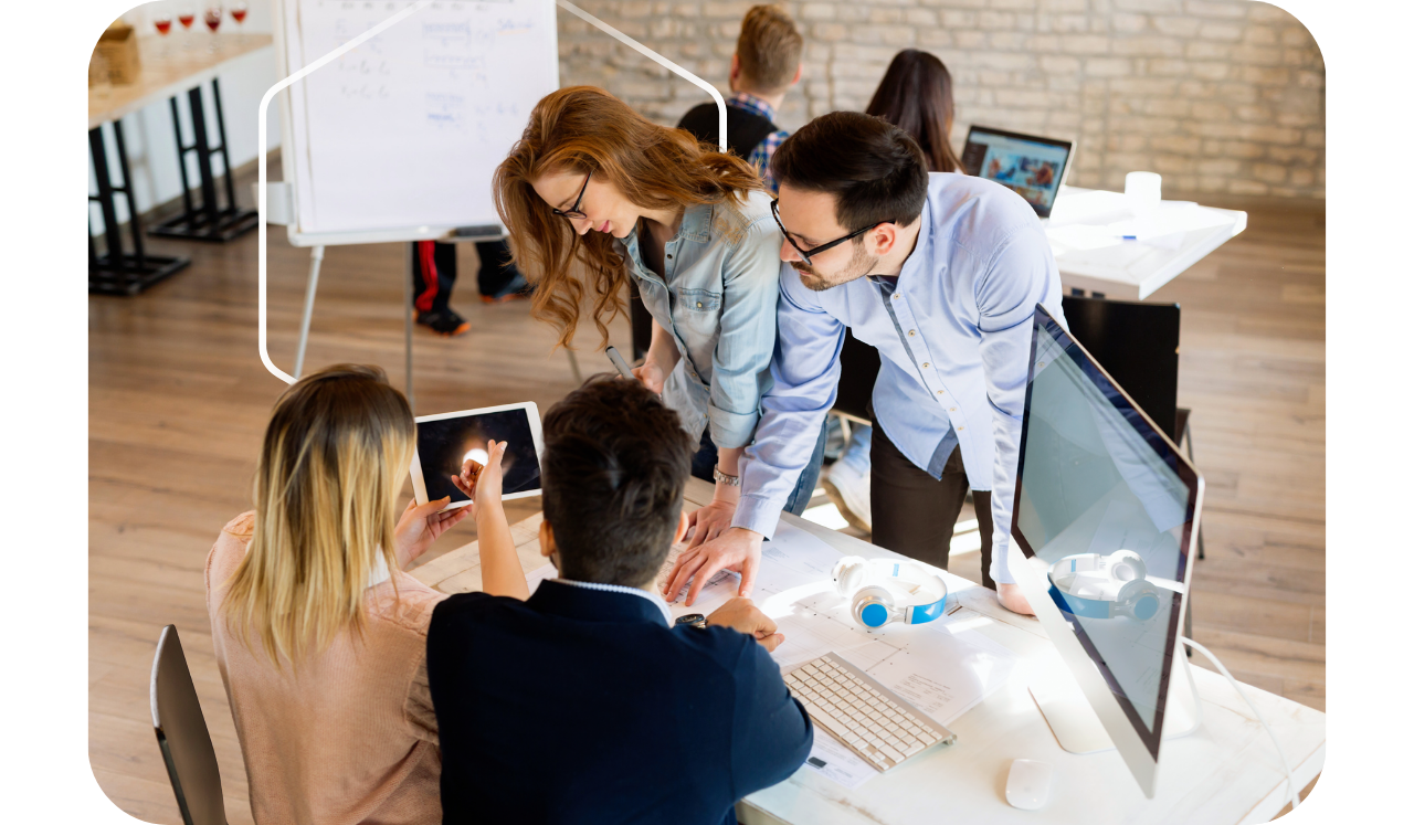 Foto de uma equipe de trabalho em um escritório realizando uma reunião em uma mesa, com um hexágono atrás deles