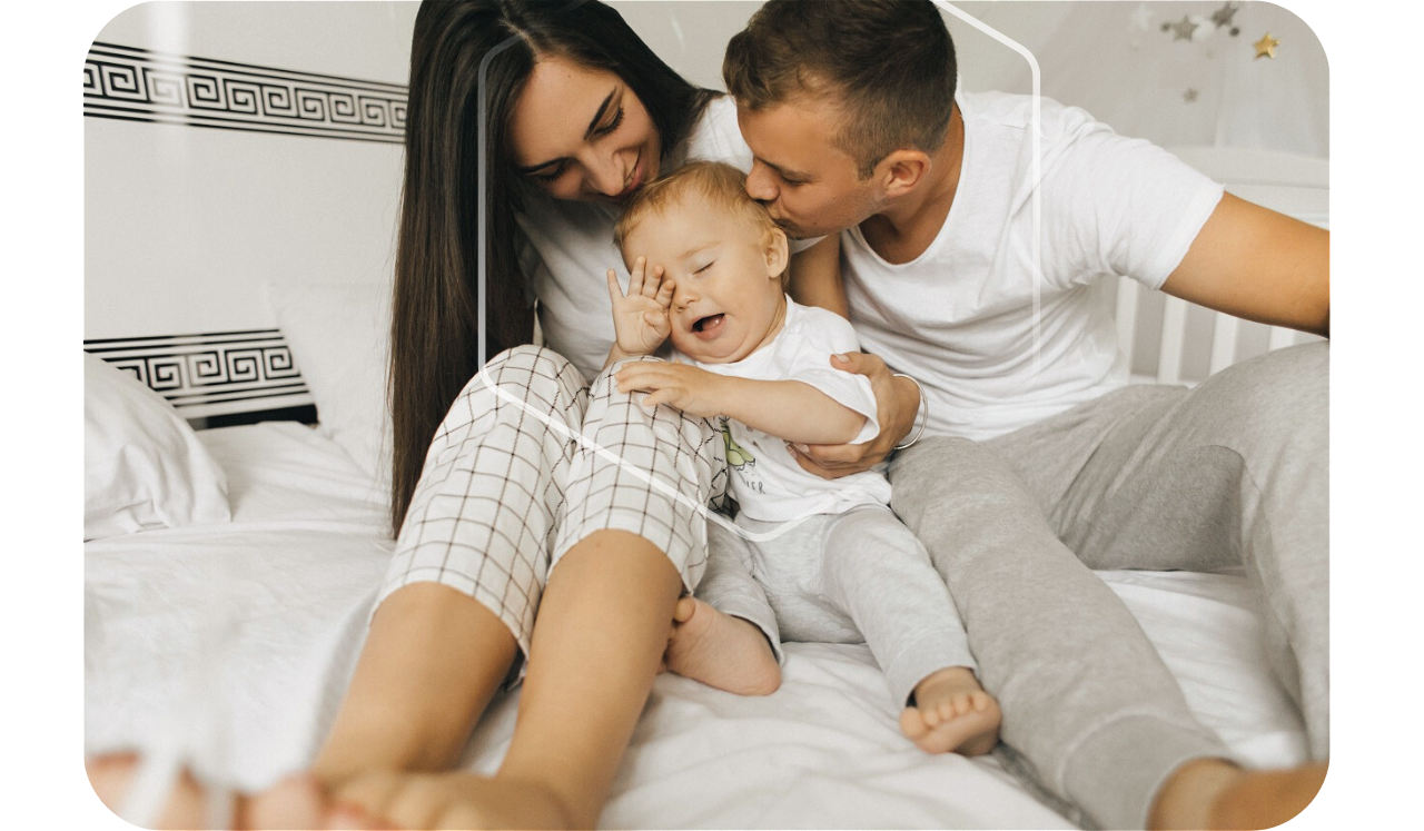 Foto de uma família, os pais e um bebê sentados em uma cama, com um hexágono em volta deles