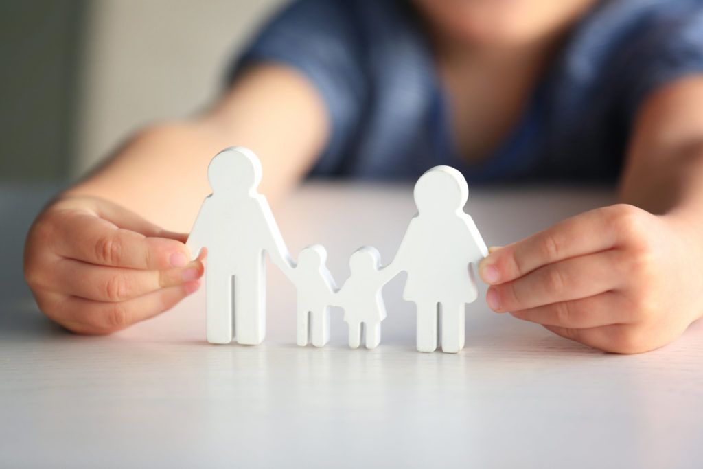 Mãos aproximando peças brancas que representam dois adultos e duas crianças de mãos dadas