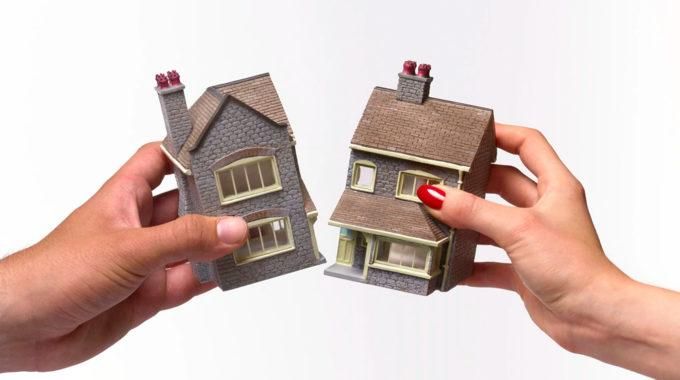 Duas mãos segurando as duas metades separadas de uma miniatura de casa