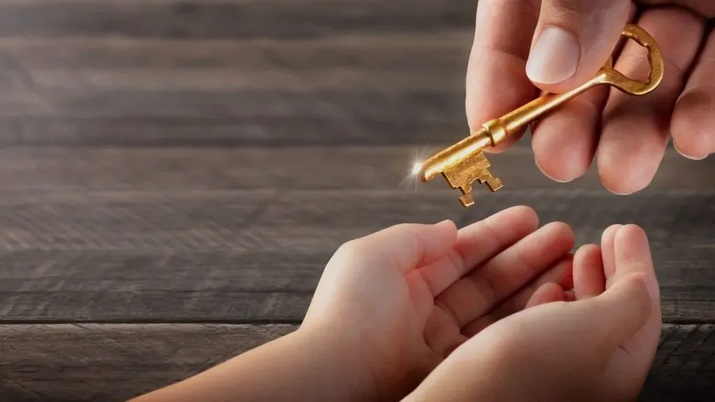 Mão de adulto entregando uma chave dourada às mãos abertas de outra pessoa