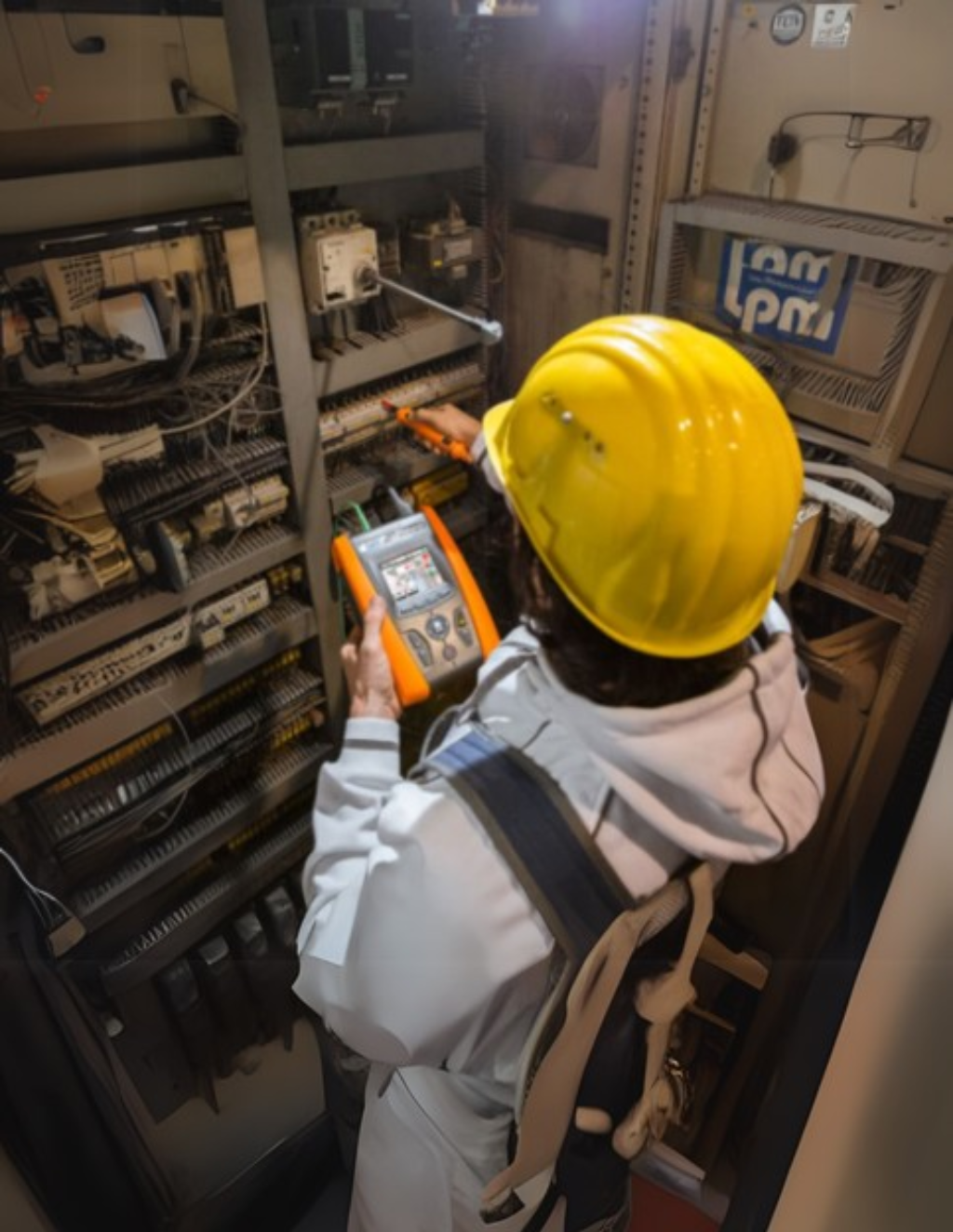 Profissional com capacete realizando medições elétricas em painel industrial usando analisador de energia portátil, representando o uso correto de instrumentos de medição elétrica para diagnóstico e manutenção preventiva.