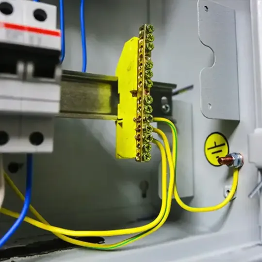 Barra de aterramento com cabos verde e amarelo conectados em quadro de distribuição industrial, destacando a importância do aterramento para segurança elétrica.
