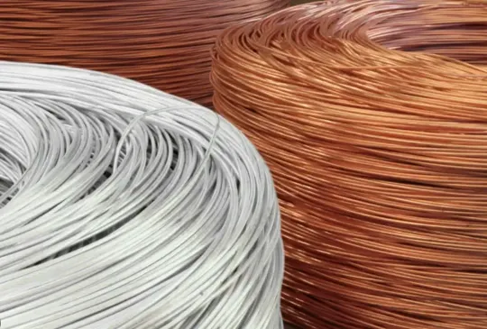 Carretéis de cabos nus de alumínio e cobre lado a lado, representando a comparação entre os dois materiais condutores utilizados em instalações elétricas. Imagem ilustrativa para entender as vantagens, aplicações e diferenças de desempenho entre cabos de cobre e alumínio.