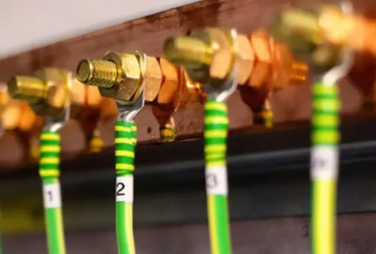 Conexões de cabos de aterramento verde e amarelo fixados em barra de cobre com terminais numerados, representando a organização e segurança dos sistemas de aterramento em painéis elétricos industriais.