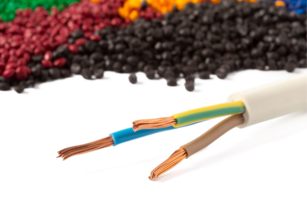 Cabo elétrico com condutores de cobre e isolação colorida em PVC, com fundo mostrando grânulos plásticos usados na fabricação de revestimentos isolantes.