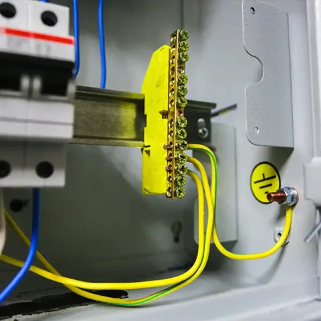 Barra de aterramento com cabos verde e amarelo conectados em quadro de distribuição industrial, destacando a importância do aterramento para segurança elétrica.