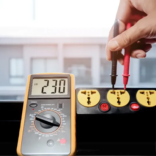 Multímetro digital medindo tensão de 230V em uma régua de tomadas, ilustrando a verificação prática de corrente elétrica para dimensionamento da bitola do cabo. Imagem utilizada no contexto de cálculo da capacidade de corrente conforme a bitola e aplicação elétrica.