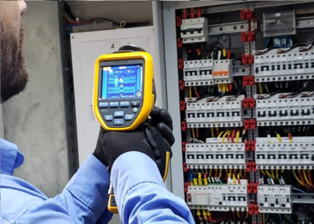 Técnico utilizando câmera termográfica para inspeção de painel elétrico industrial, identificando aquecimentos e prevenindo falhas como parte da manutenção preventiva
