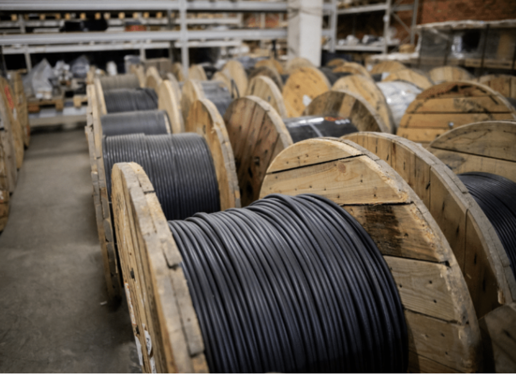 Bobinas de madeira com cabos elétricos enrolados em diferentes bitolas armazenadas em estoque industrial, ilustrando a variedade de cabos utilizados em instalações elétricas residenciais, comerciais e industriais conforme a corrente e a aplicação.